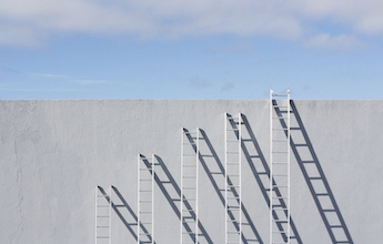 Five white ladders of increasing heights rest against a wall.