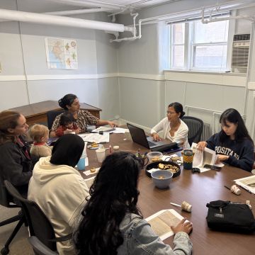 Group photo of women and children having a discussion around a table.