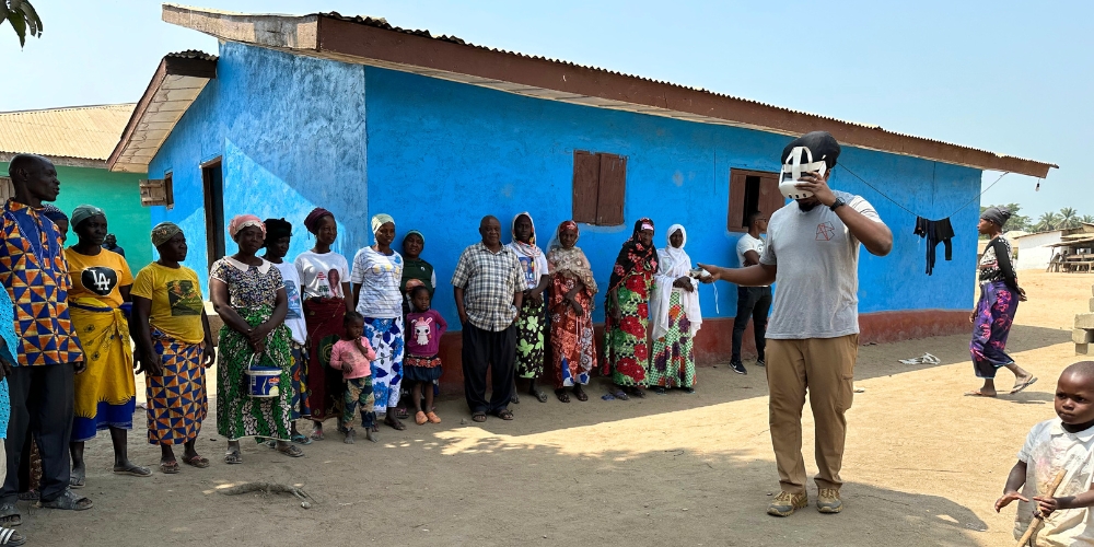 Stevens preparing for a VR demonstration as residents look on with a mix of excitement and skepticism. (Sarkonedu, Liberia)