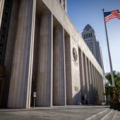 A large courthouse building with tall stone columns stands in the foreground, while an American flag waves on a pole to the right.