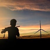 Silhouette of a child playing a flute in front of windmills with a sunset in the background.  